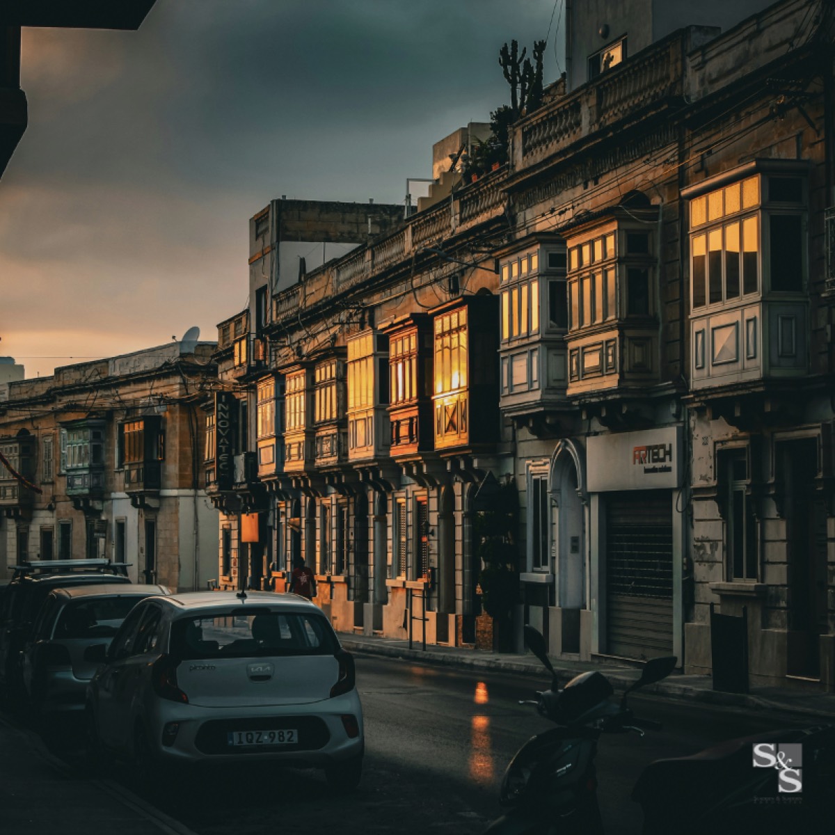 Traditional Maltese enclosed timber balconies lit at dusk along a Birkirkara street.